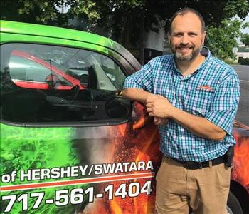 General Manager Jason Roberts (male with brown hair) smiling and leaning on SERVPRO marketing car 