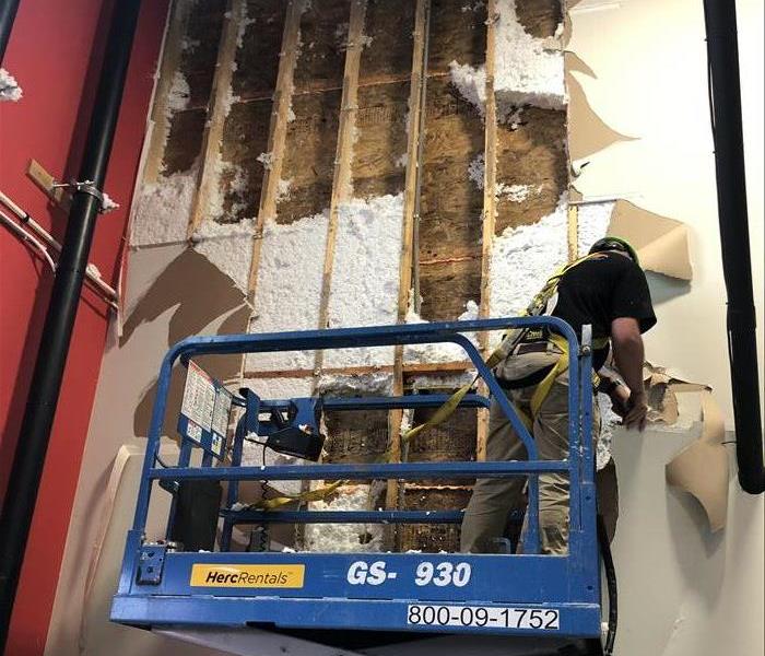 Technician on a scissor lift removing insulation and drywall