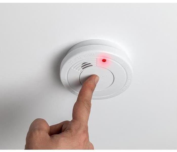 Finger pressing button on smoke detector
